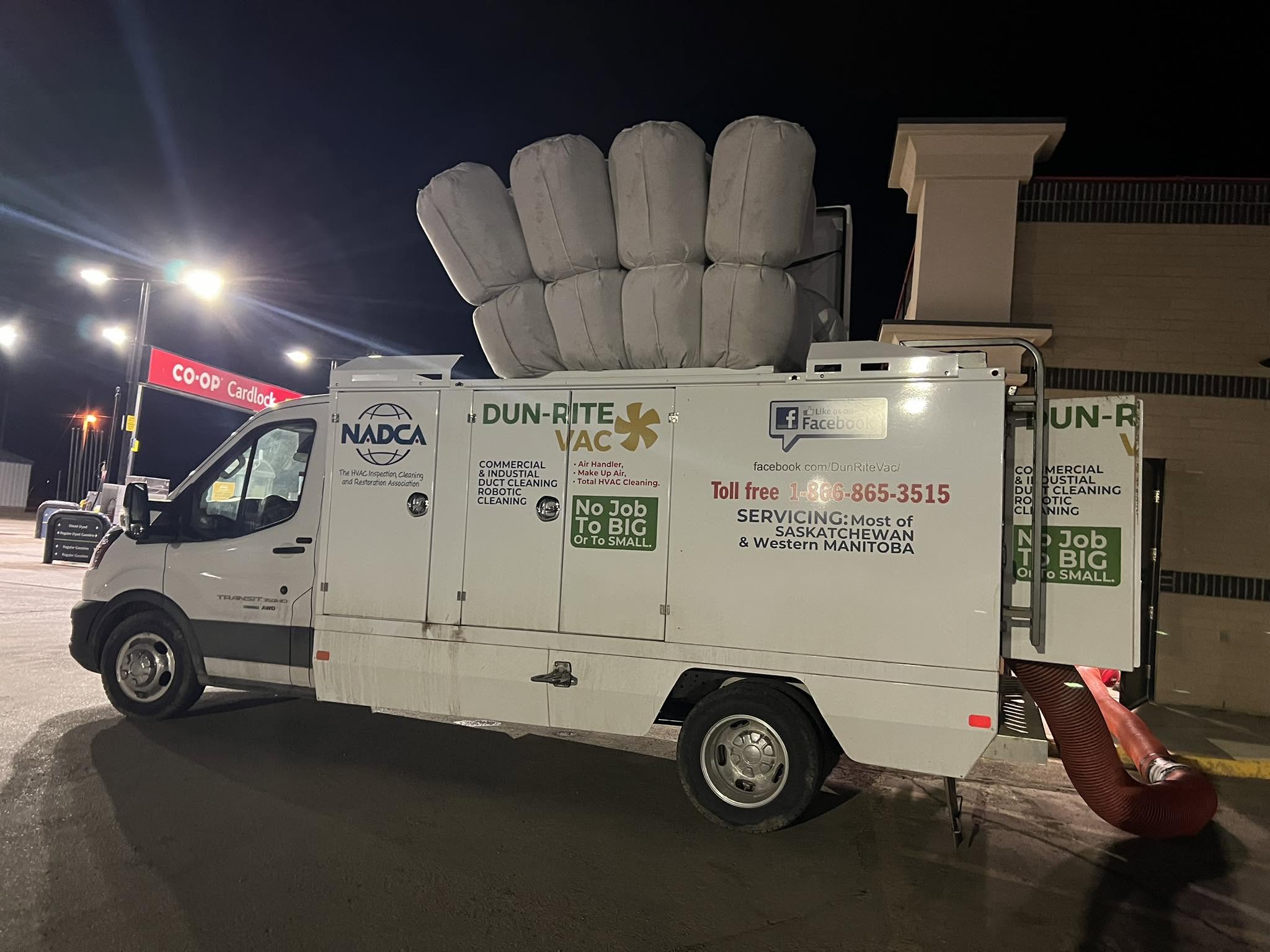 Dun-Rite Vac service van with vacuum hose connected, parked outside a building at night